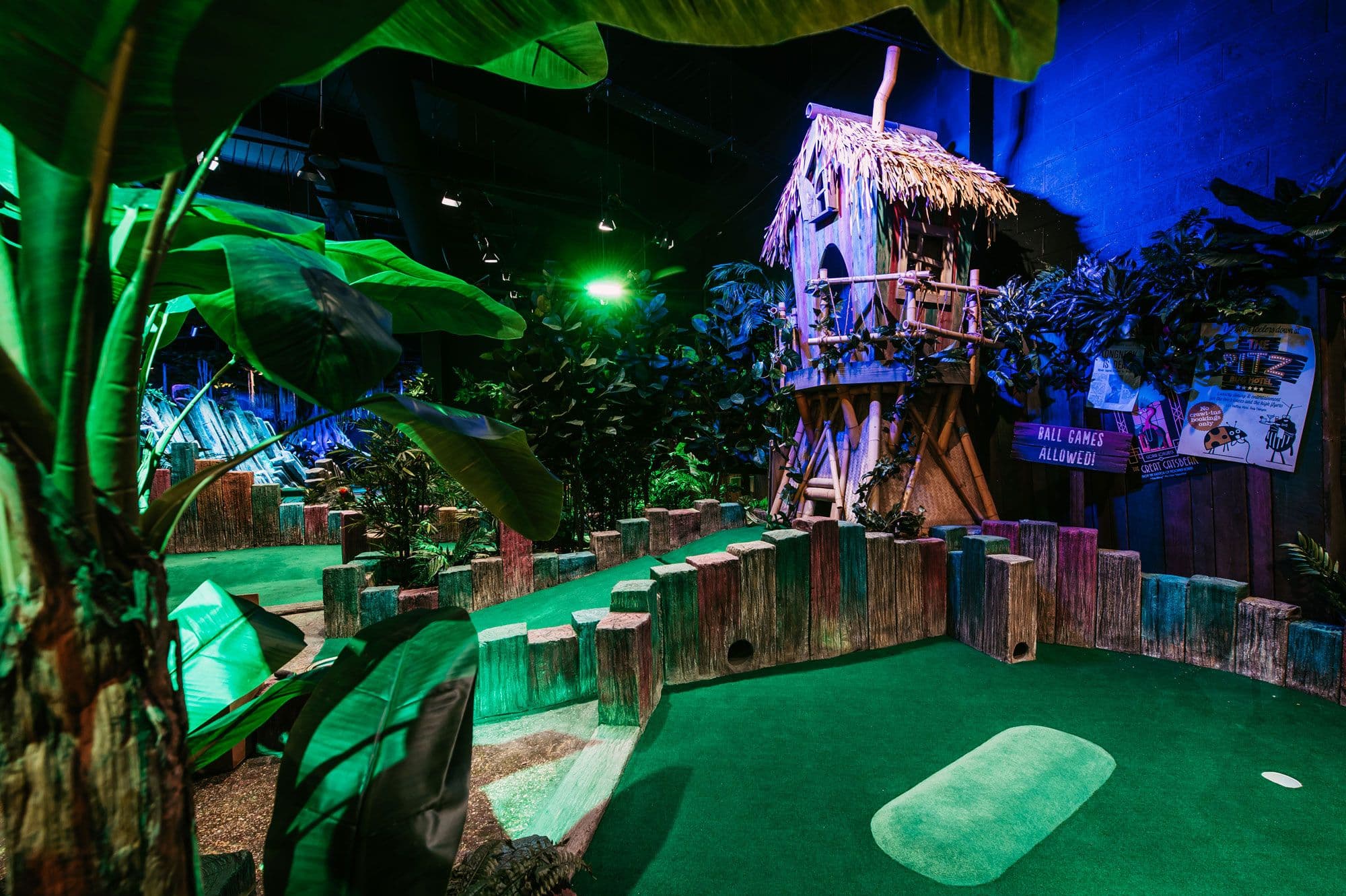 Bright image of the Twee-T Tower birdhouse hole, with a large wooden green and red house, thatched roof and thick jungle foliage around.