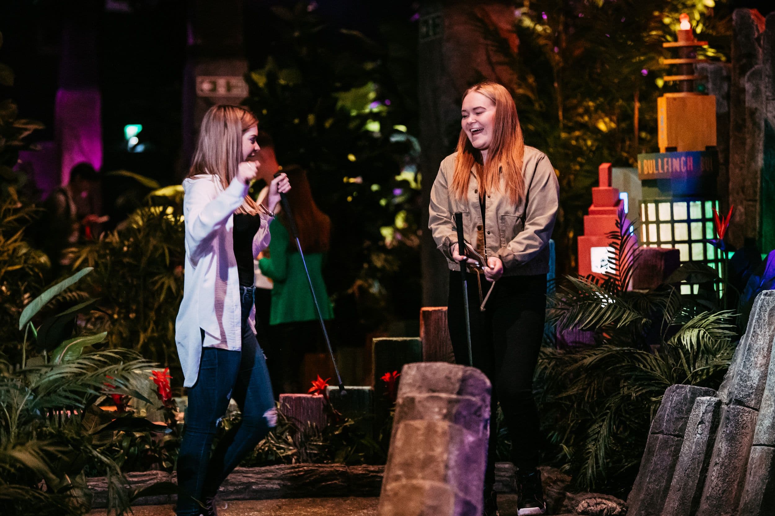 Two yGirls laughing playing mini golf.